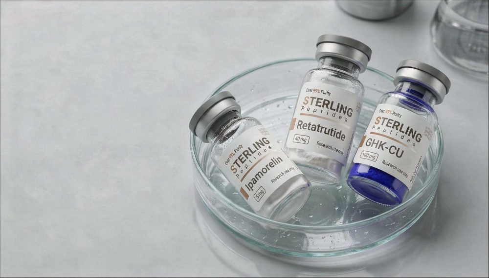 Three Sterling Peptides vials labeled Retatrutide, Ipamorelin, and GHK-CU sit in a glass bowl with a few droplets of liquid, suggesting a pharmaceutical research setting.